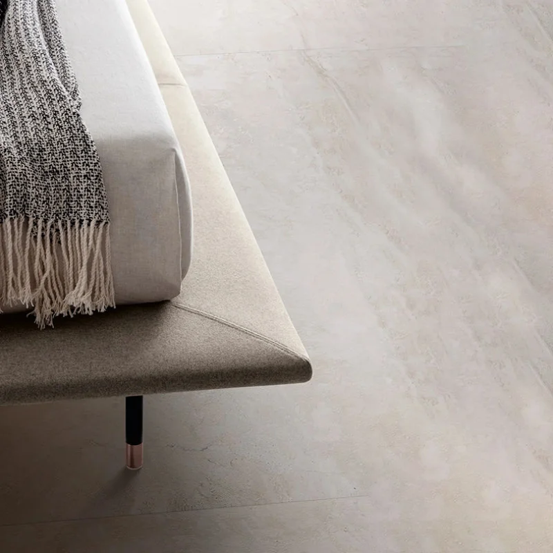 Beige sofa edge with a fringed knit blanket draped over the arm and a dark leg visible beneath the seat