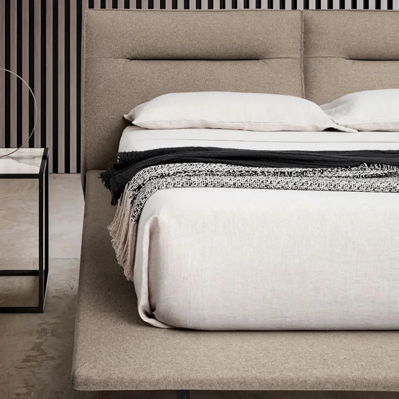 Bed with beige upholstered headboard, white linens, and a textured throw blanket in a modern bedroom setup with a glass-topped nightstand nearby