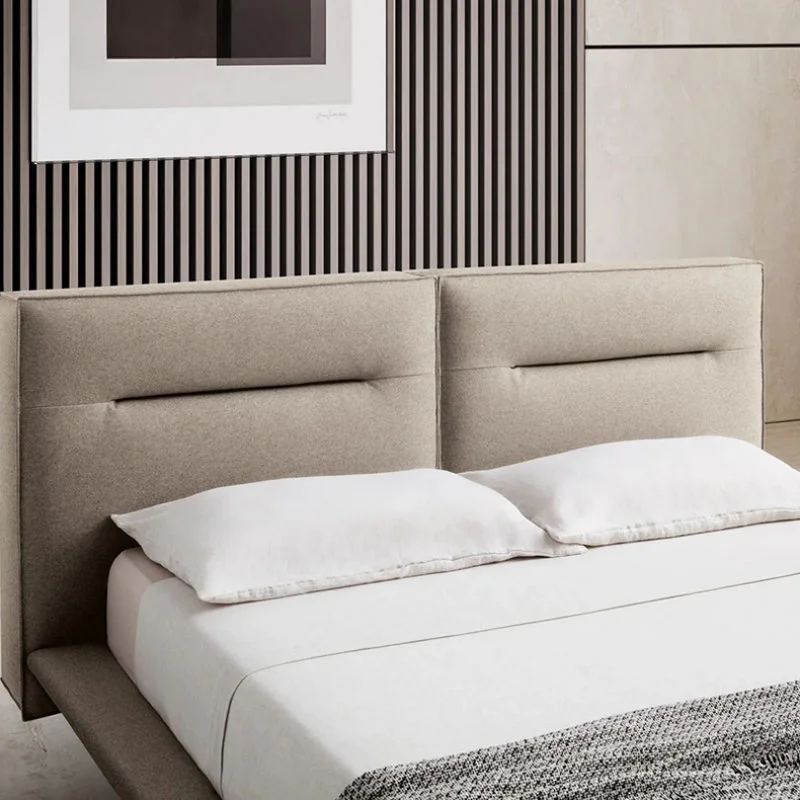 Beige upholstered bed with two white pillows and white sheets, against a striped vertical-panel wall with a framed abstract art piece above.