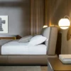 Hotel bedroom with a king bed, gray upholstered headboard, white linens and pillows, and warm bedside lamps.