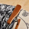 Close-up of a wooden chair armrest with a metal frame, resting on a black-and-white patterned fabric and a beige rug.