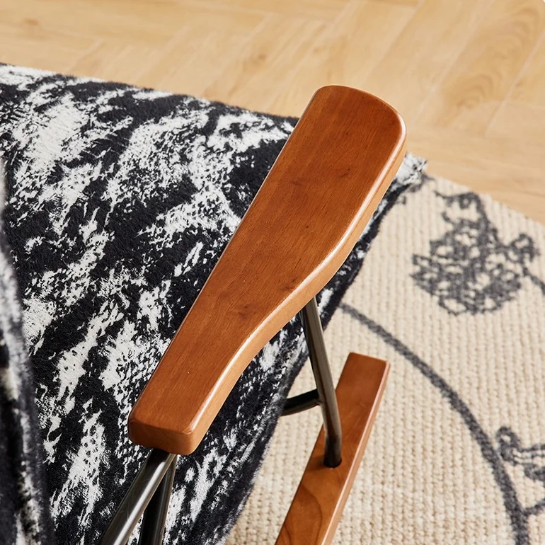 Close-up of a wooden chair armrest with a metal frame, resting on a black-and-white patterned fabric and a beige rug.